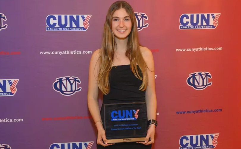 Paz Moran holds the 2026 CUNYAC Female Scholar-Athlete of the Year plaque in front of backdrop with CUNY athletics logos.