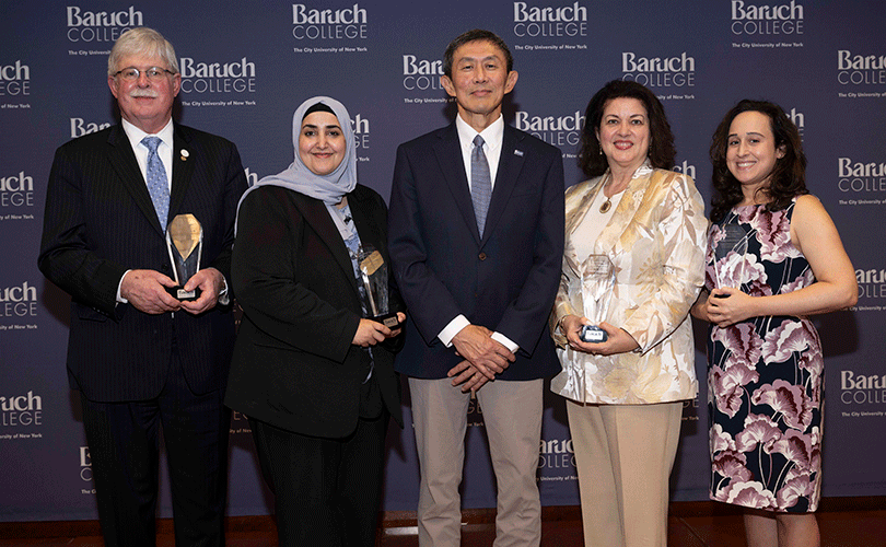 Group portrait at a Baruch College event featuring five people standing side by side, with four recipients holding crystal recognition awards against a branded college backdrop.