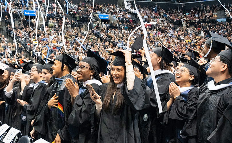 Group of students smiling at a Baruch College Commencement Ceremony with streams of confetti in the air.