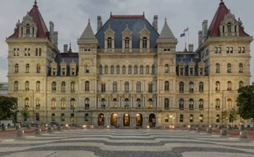 Front view of the New York State Capitol in Albany, a historic stone government building with ornate towers and a large patterned plaza in the foreground.