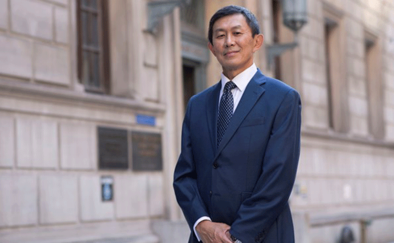 Baruch College President S. David Wu standing in front of a campus building wearing a navy blue suit.