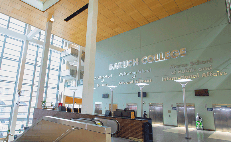 Interior lobby of Baruch College&rsquo;s Newman Vertical Campus building with escalators, elevators, and large wall signage displaying the school names.